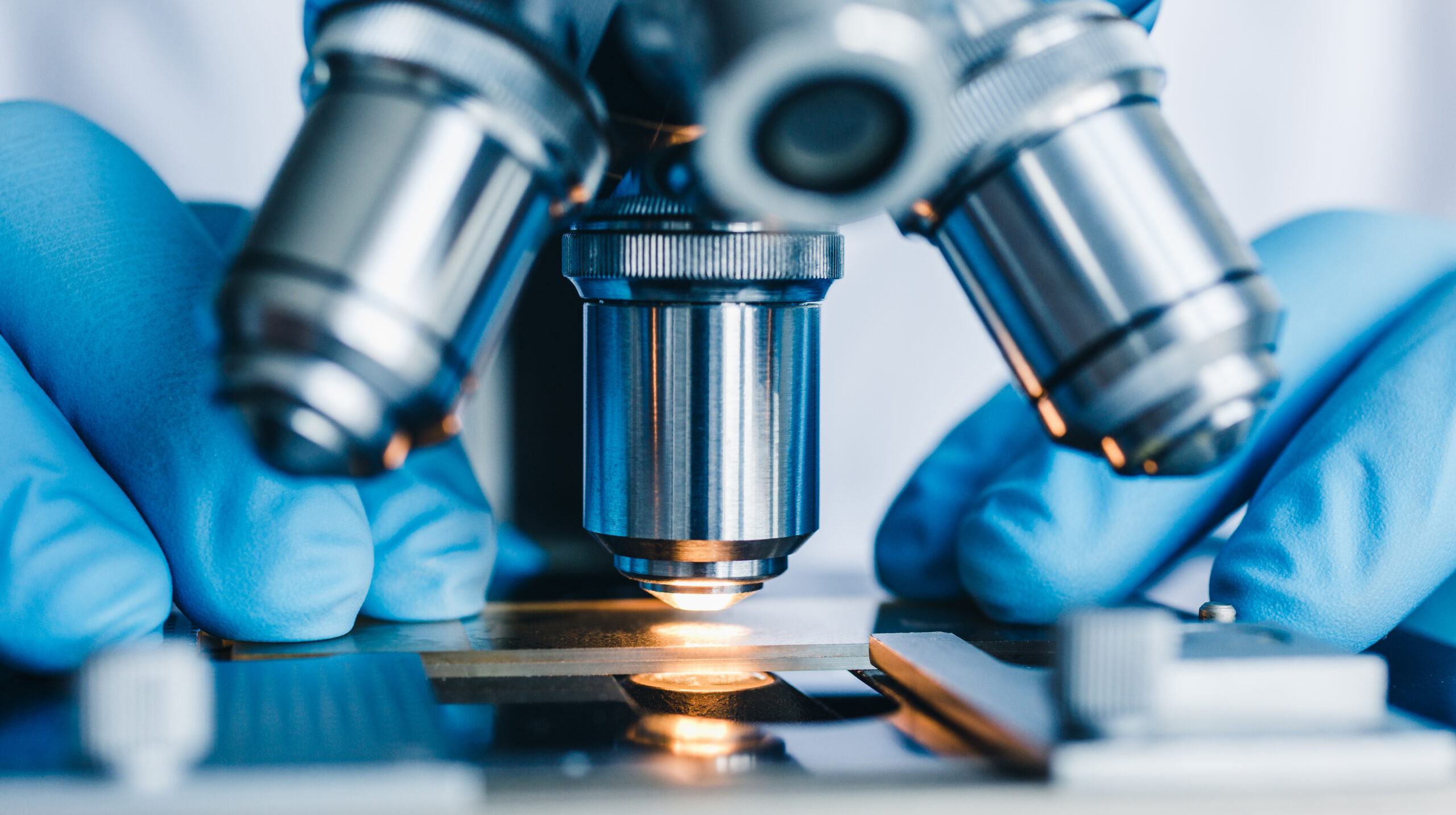 Close-up of gloved hands adjusting a microscope slide in a laboratory.