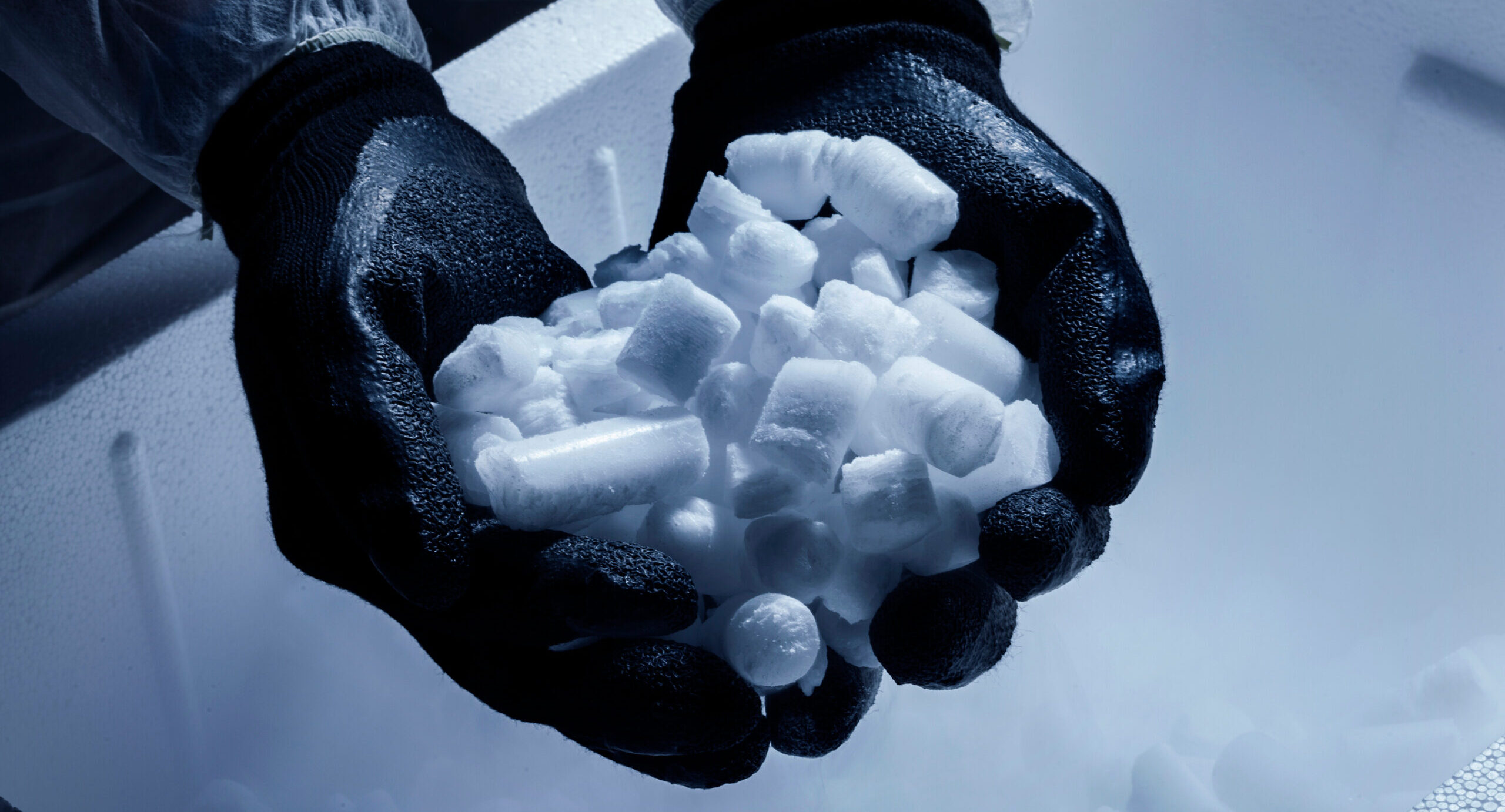 Gloved hands holding dry ice pellets used in product supply logistics.